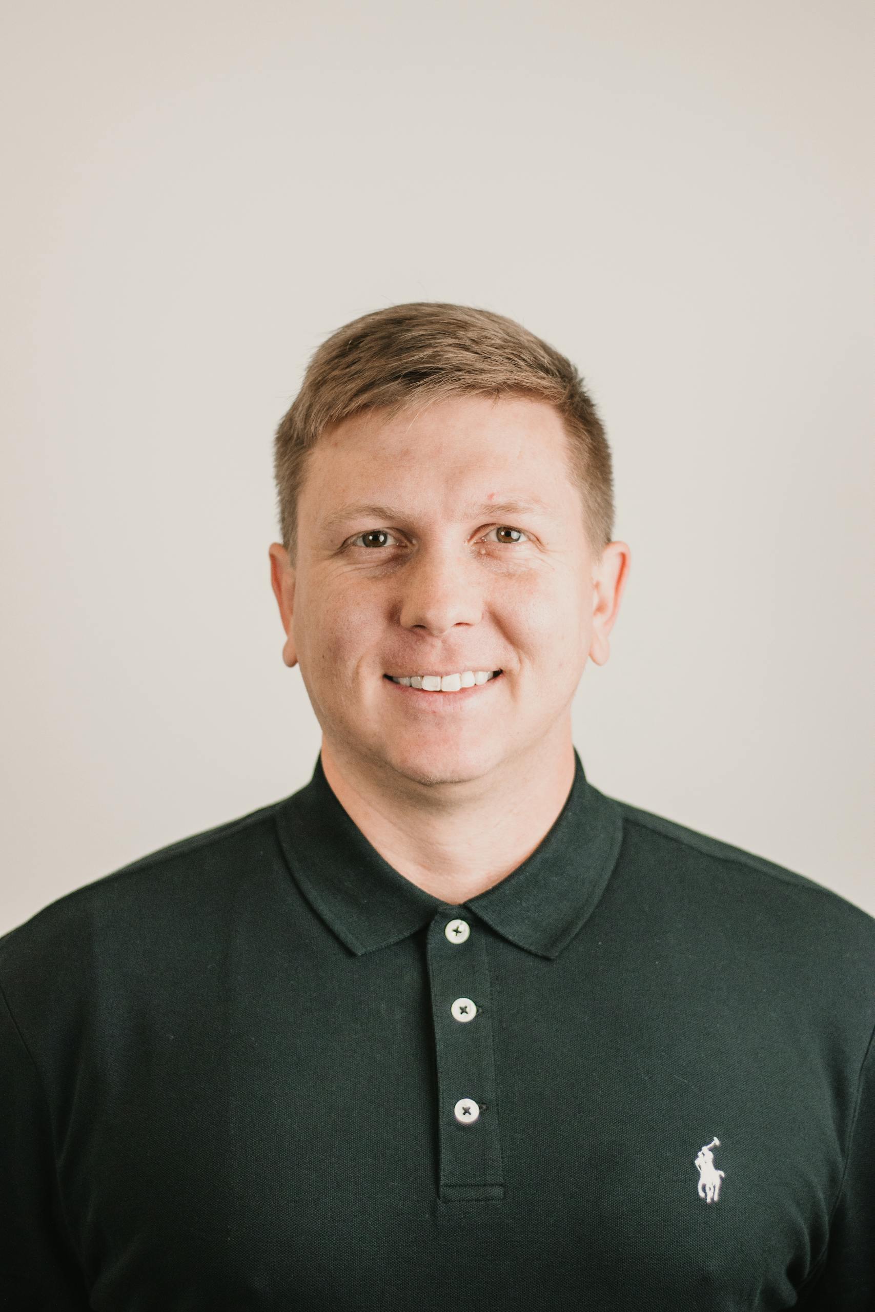 A polished headshot of a smiling man in a dark polo shirt, ideal for business or personal use.