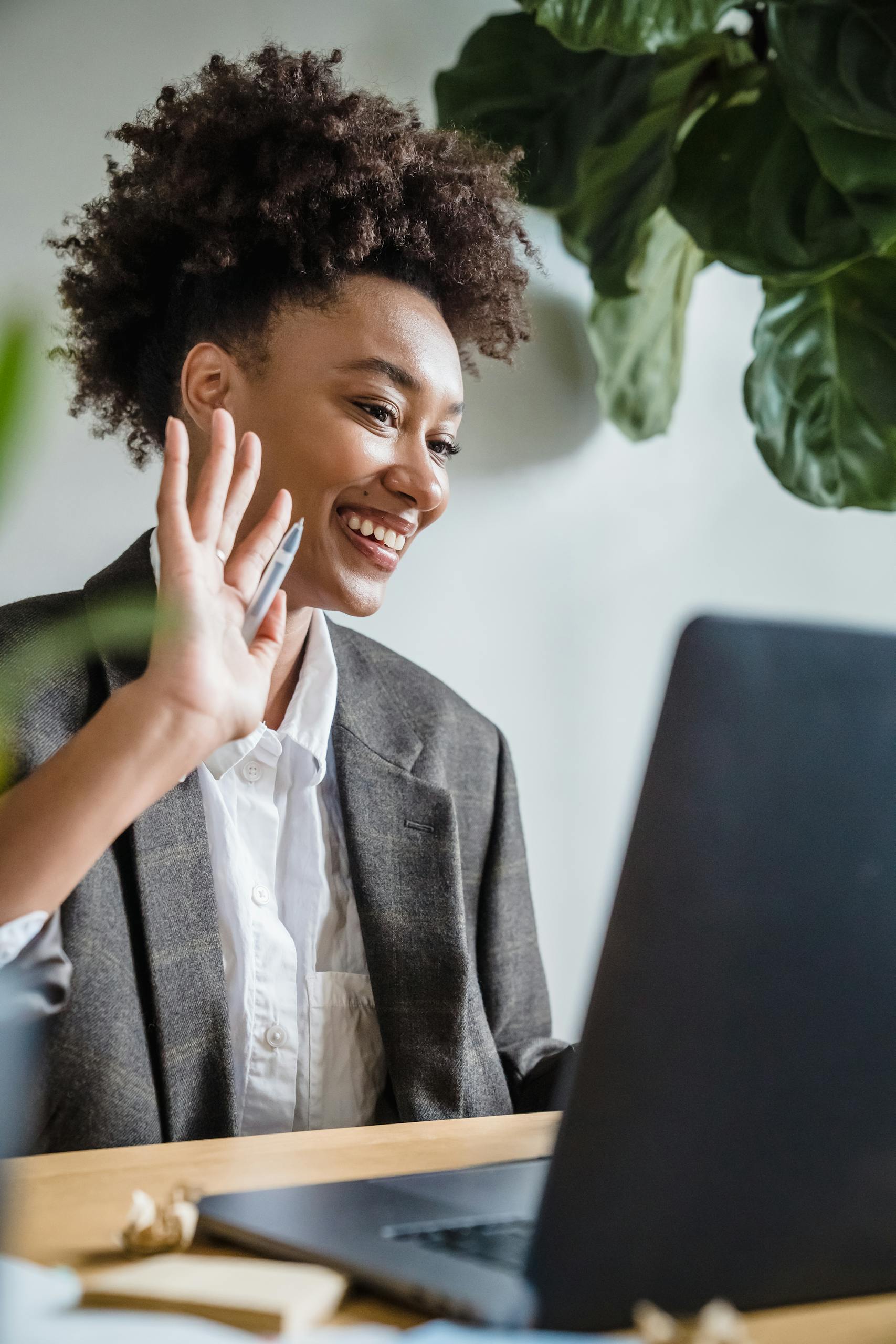 Cheerful businesswoman waving during a remote video call in a modern home office.