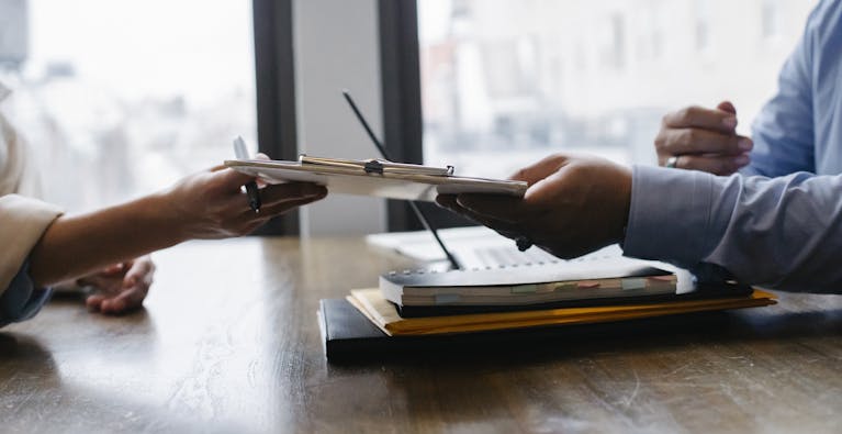 How to Write a Job Description: Template, Example and Compliance Tips 2 Crop anonymous ethnic woman passing clipboard to office worker with laptop during job interview