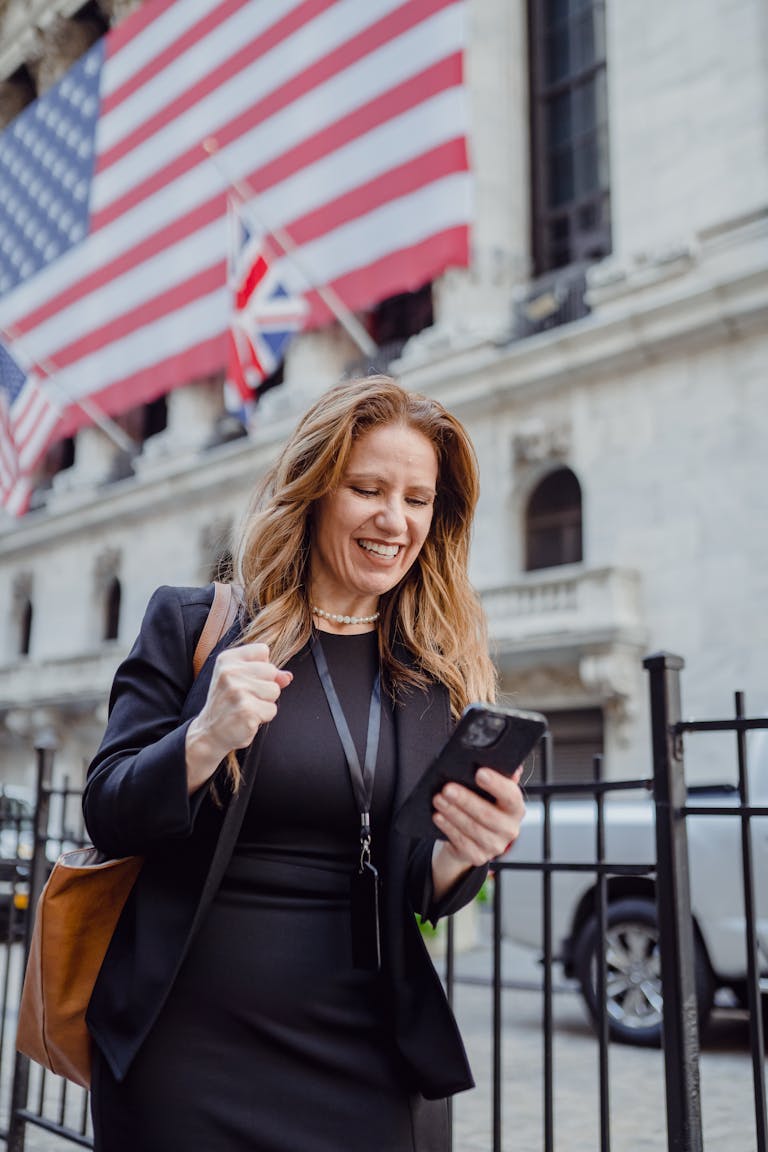 Cheerful businesswoman celebrating good news while walking outside a historic building with flags.