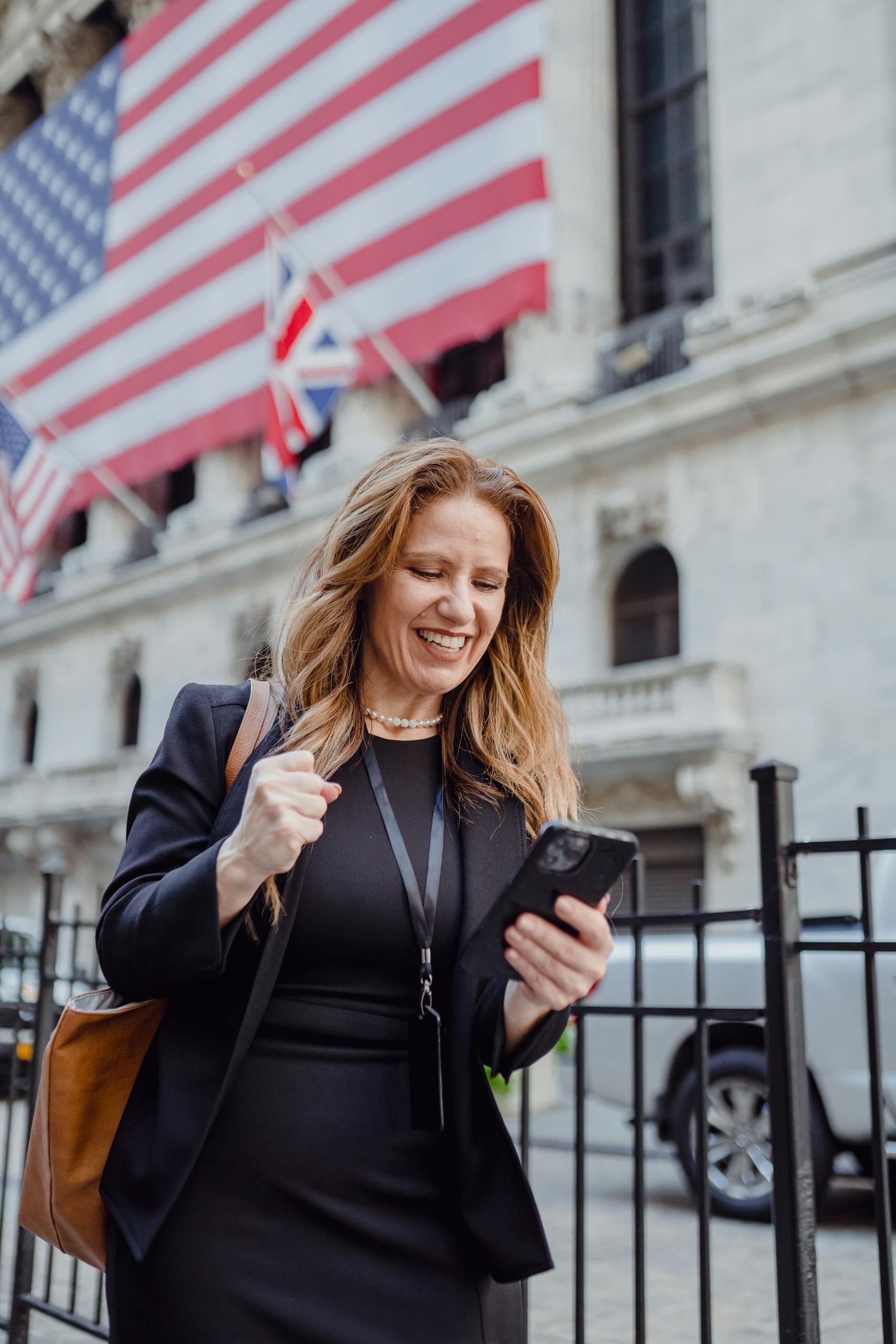 Cheerful businesswoman celebrating good news while walking outside a historic building with flags.