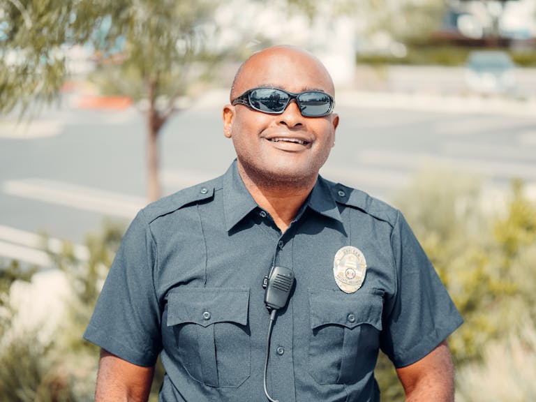 Portrait of a smiling police officer outdoors wearing sunglasses and uniform.