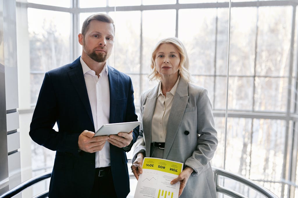 Two business professionals in a modern office discussing a project with a tablet and report.