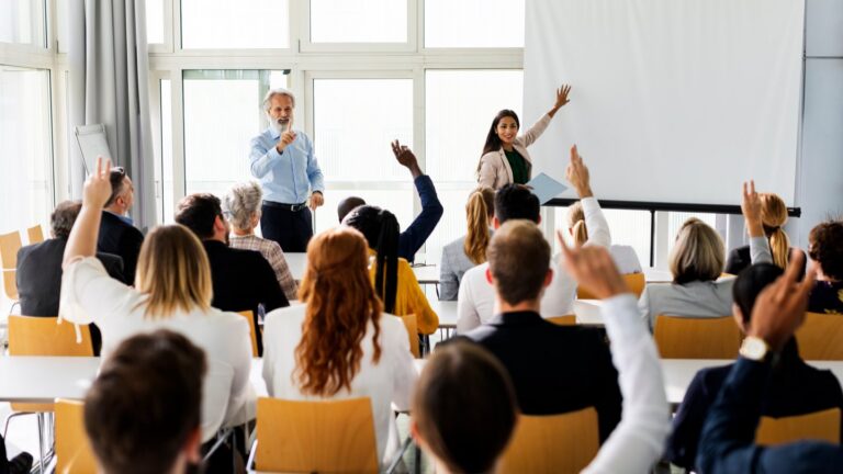 New managers raising their hands in a leadership training class as part of a fall manager training program