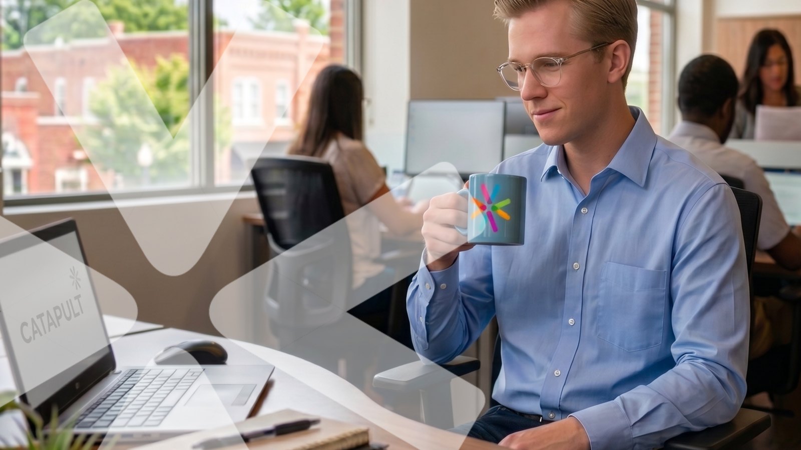 An employee reviews work on a laptop in a Catapult office, holding a mug with the Catapult spark mark.